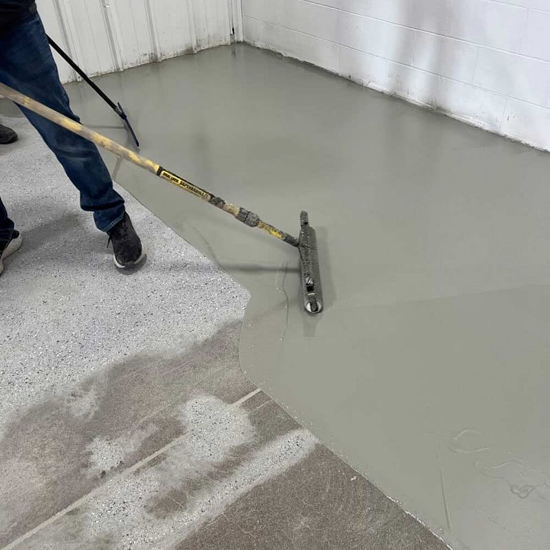 A person applying a base coat to a concrete floor.