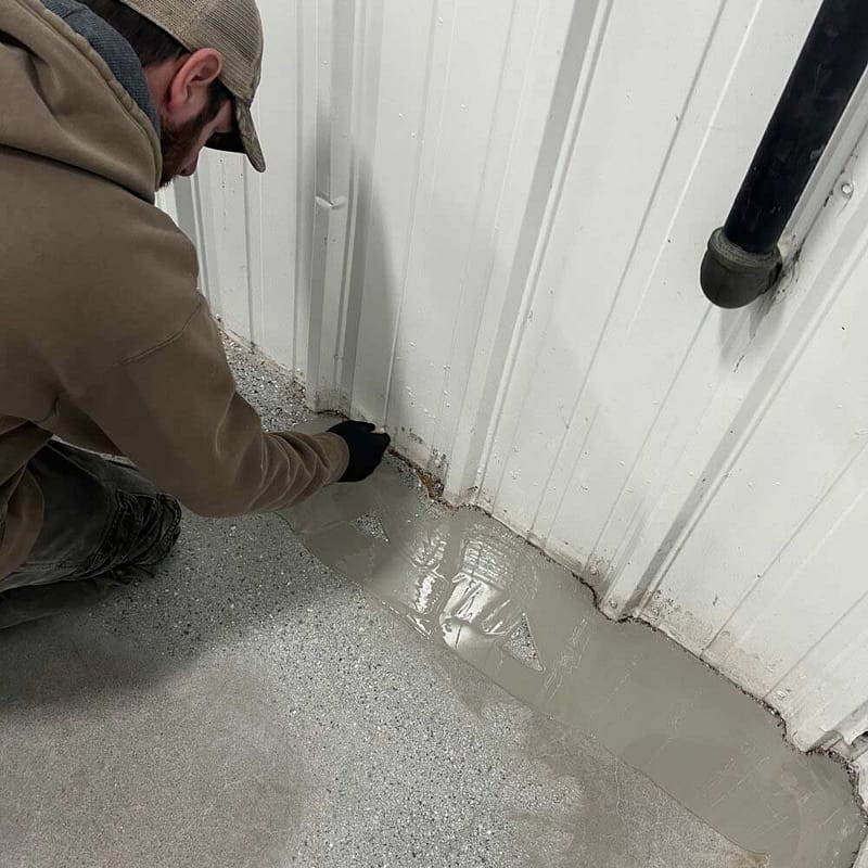 A man applying a base coat around the edge of a concrete floor.